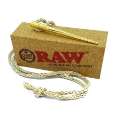Zlaté šťouchátko s raženým logem RAW položené na prezentační krabičce, kolem pletená konopná šňůrka.