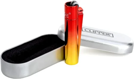 Červeno-oranžovo-žlutý kovový Clipper opřený o otevřenou stříbrnou plechovou krabičku s logem CLIPPER